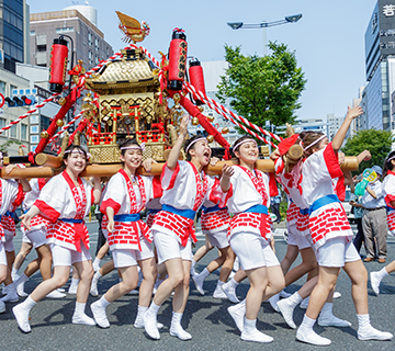 A group of women carry a golden mikoshi through the streets at a festival.