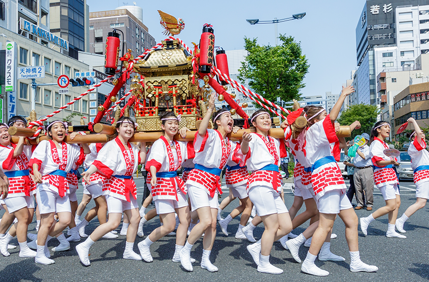 A group of women carry a golden mikoshi through the streets at a festival.