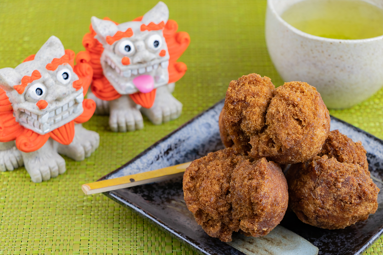Okinawa Shisa lion-dogs sit on a green table next to Okinawa brown sugar dontus.