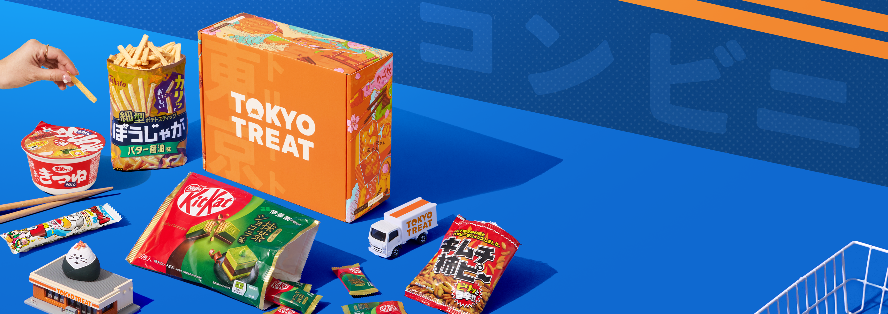 Orange TokyoTreat box on blue background with konbini-themed snacks around it 