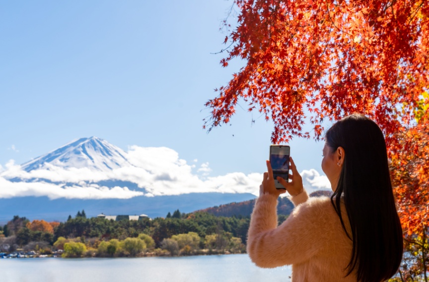 Asian woman taking a picture from afar of Mt. Fuji during the fall 