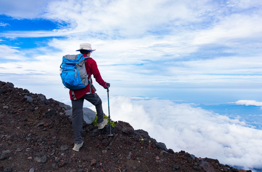 Asian man hiking on top Mt. Fuji, overlooking the clouds