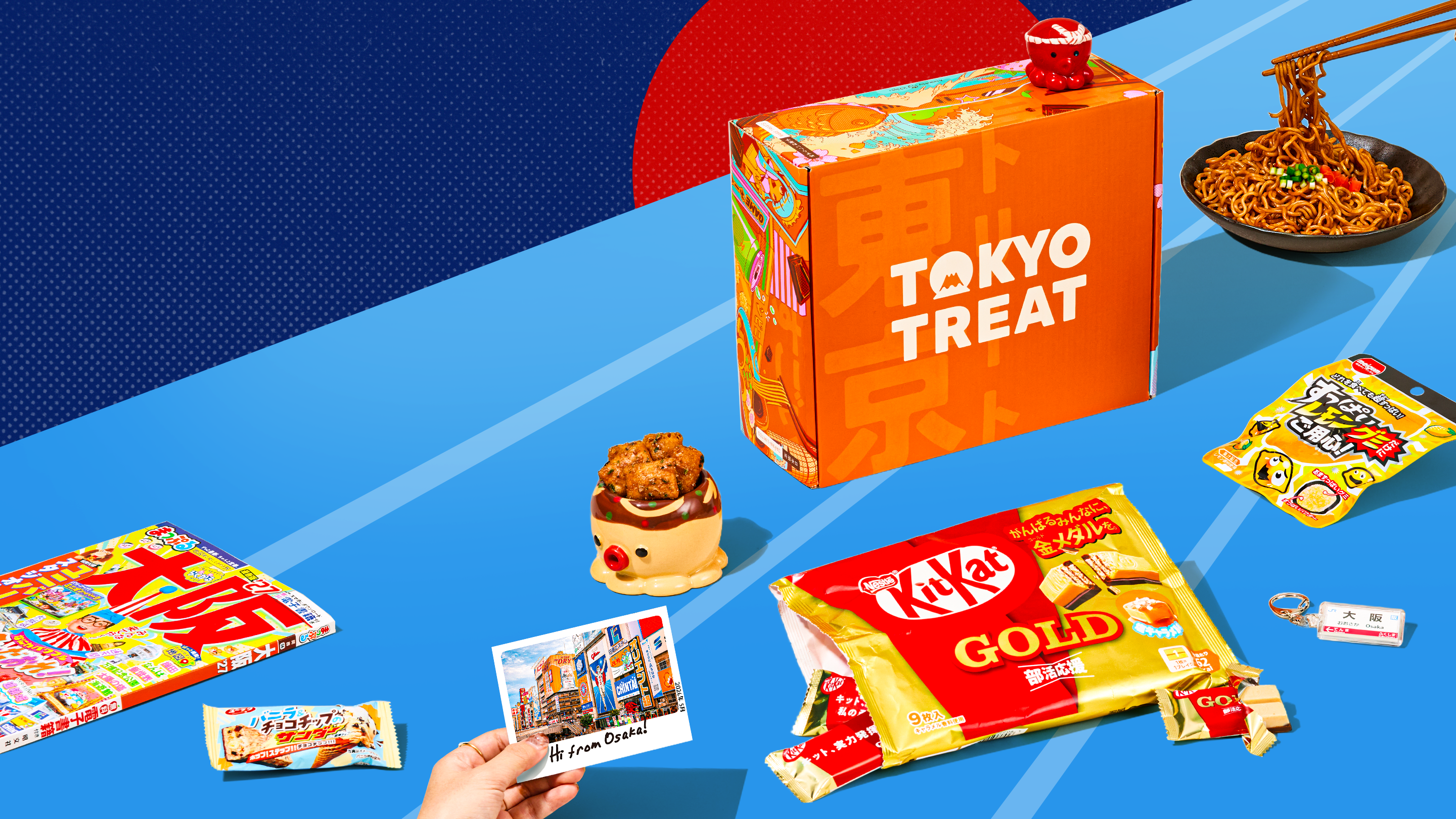 Orange TokyoTreat box with Osaka-themed snacks on blue background with red sun in the back