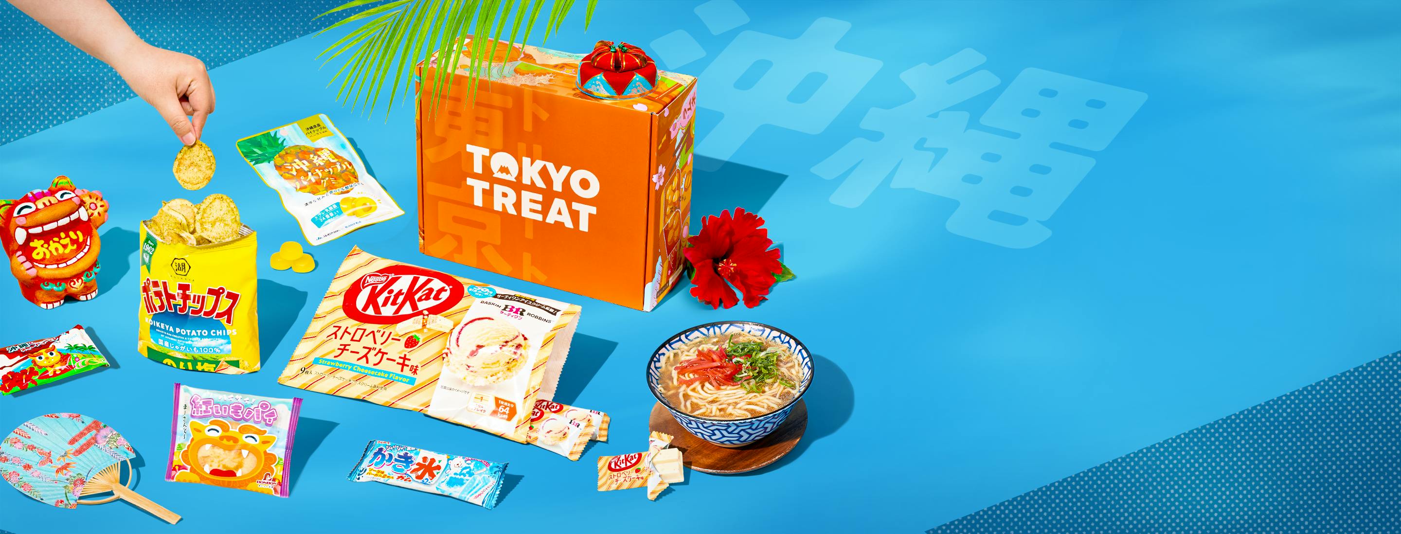 Orange TokyoTreat box on blue background with Okinawa-themed snacks around it