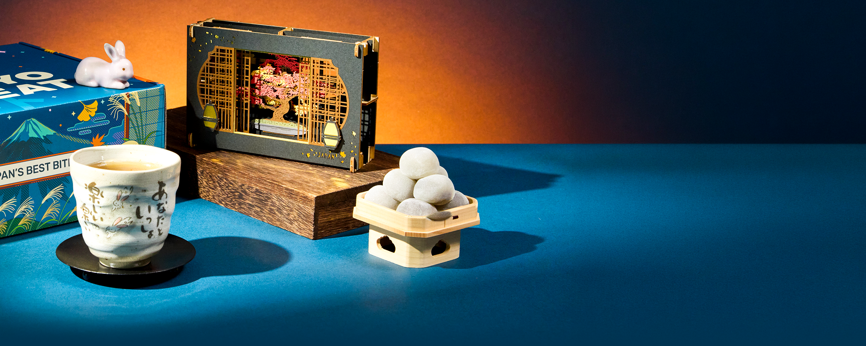 Mochi, a tea cup, and papercraft diorama on a blue background
