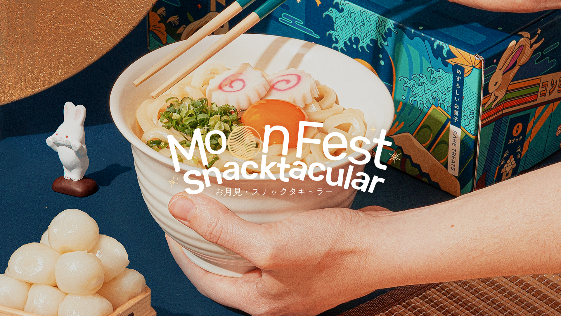 A pair of hands holds a bowl of Tsukimi udon, surrounded by Tsukimi Moon Festival decorations.