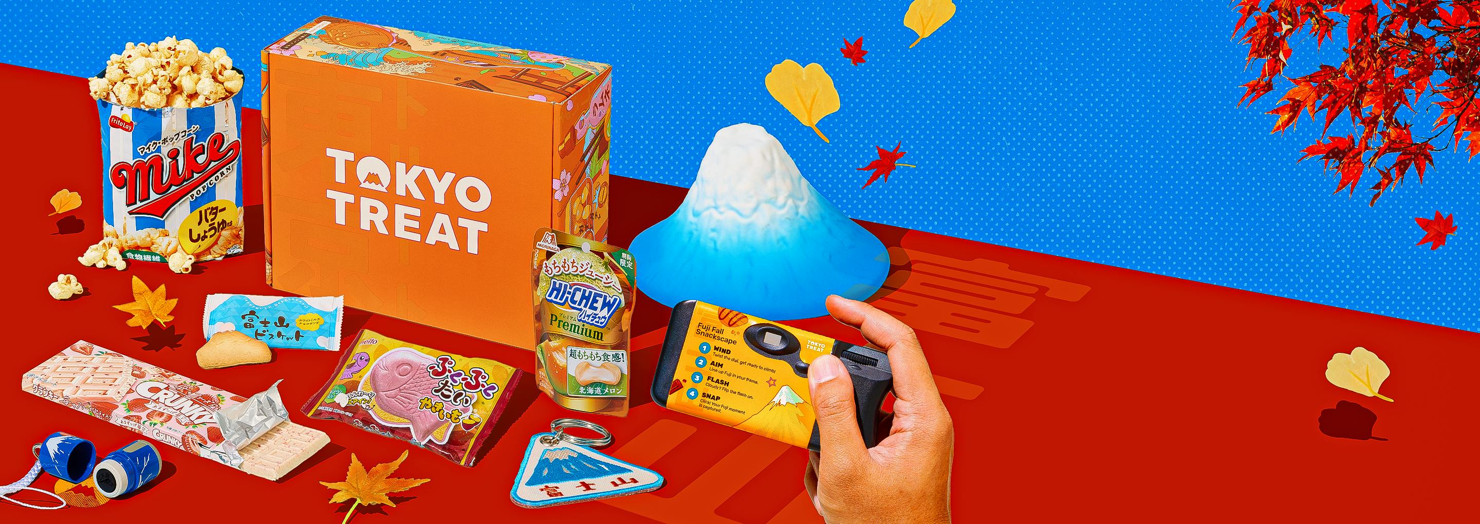 Orange TokyoTreat box with fall snacks around it on red background with Mt. Fuji figurine