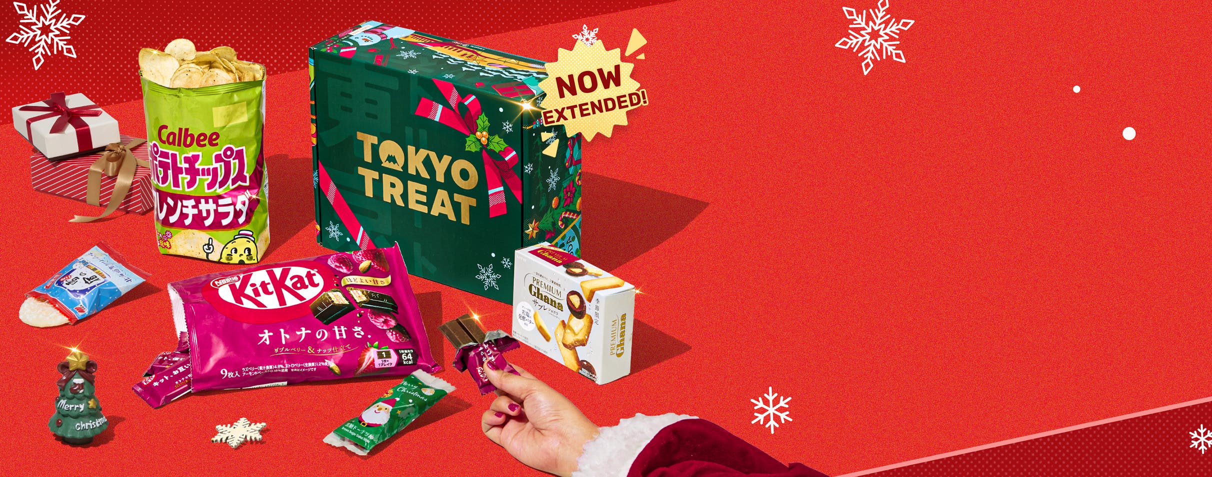 Green TokyoTreat holiday box on red background with snowflake ornament and Christmas themed snacks around it