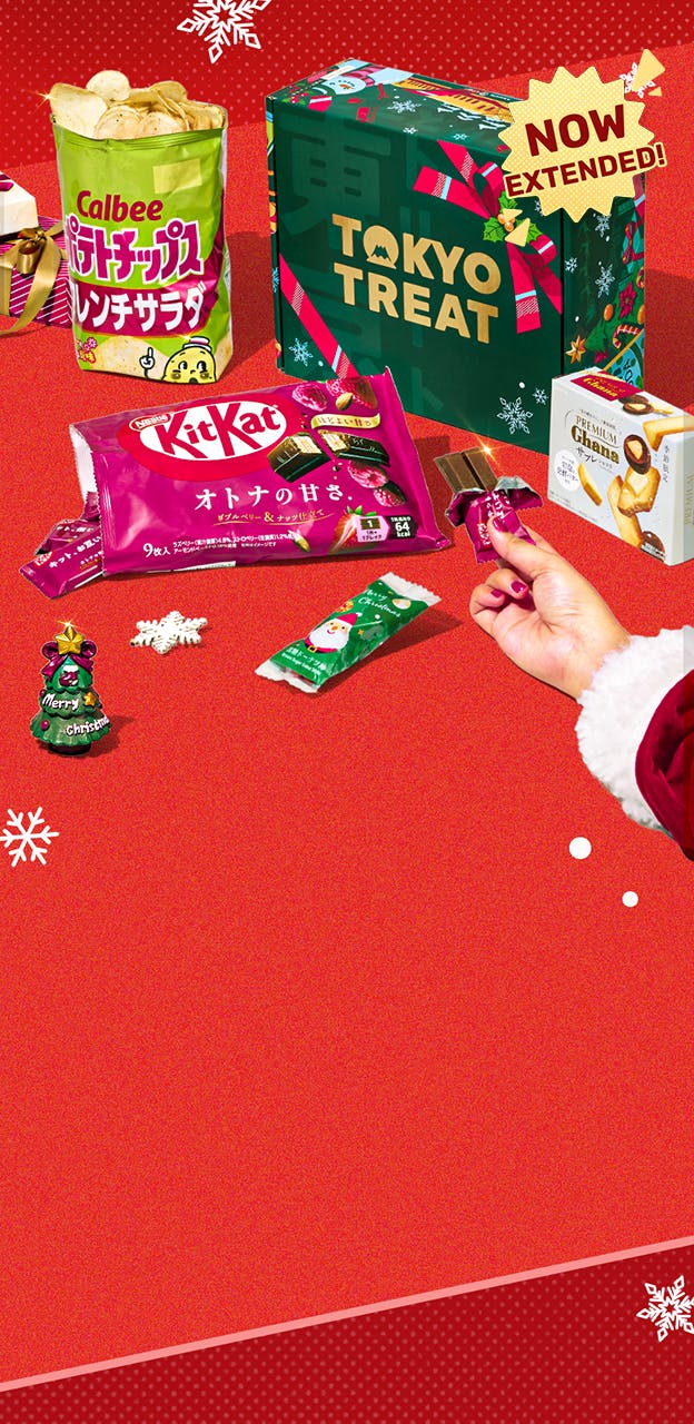 Green TokyoTreat holiday box on red background with snowflake ornament and Christmas themed snacks around it