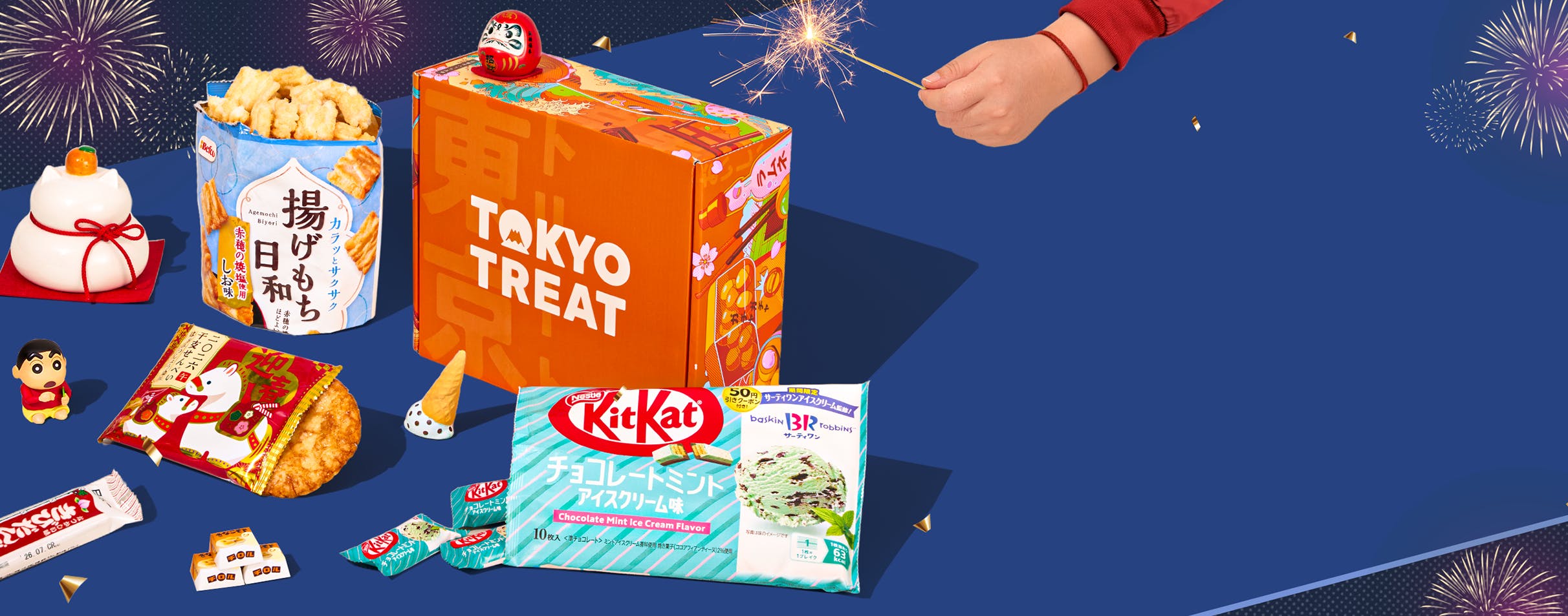 Orange TokyoTreat box on blue background with Japanese New Year-themed snacks with maneki neko figure