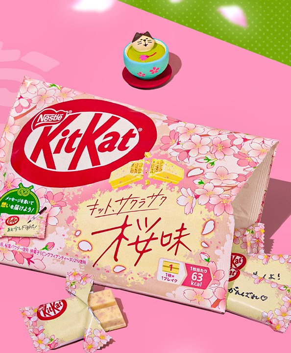 Bag of sakura KitKats on pink background with figurine of cat bathing inside a matcha cup