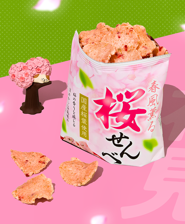Bag of sakura shrimp rice crackers on pink background with figurine of cat resting on branch of cherry blossom tree