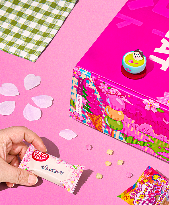 Hand holding sakura KitKat next to pink TokyoTreat box on pink background