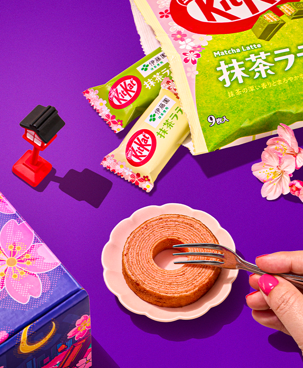 Sakura roll cake on plate with Matcha Latte KitKats around it on purple background